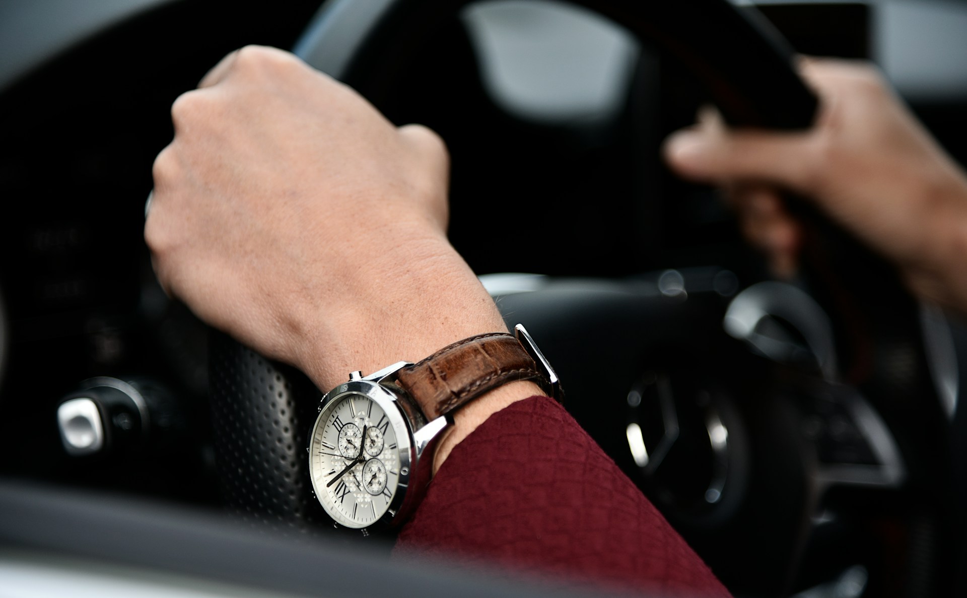 a person&rsquo;s hands holding a steering wheel and adorned with a luxury watch