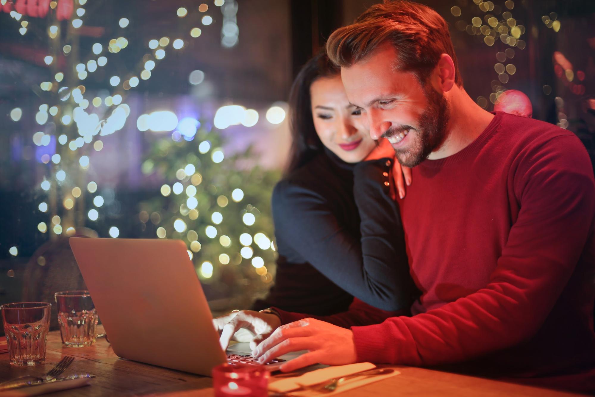 A smiling couple on a date sits at a wooden table in a cozy ambient café lit by warm fairy lights.