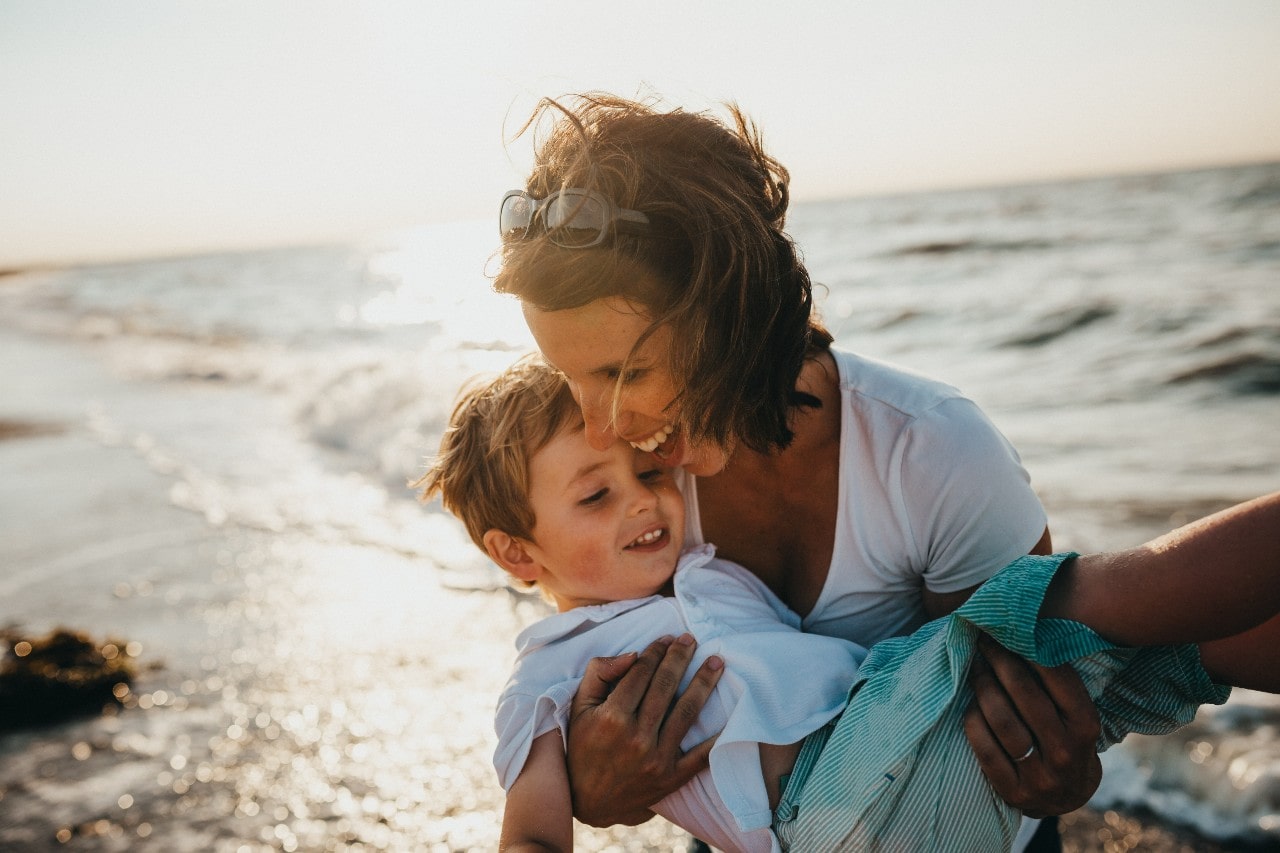 A joyful mother holding her son on the sunlit beach.