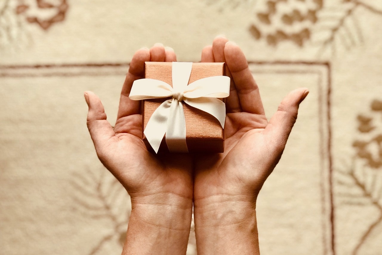 A close-up view of a person’s hands carefully holding a small gift box in their palms.