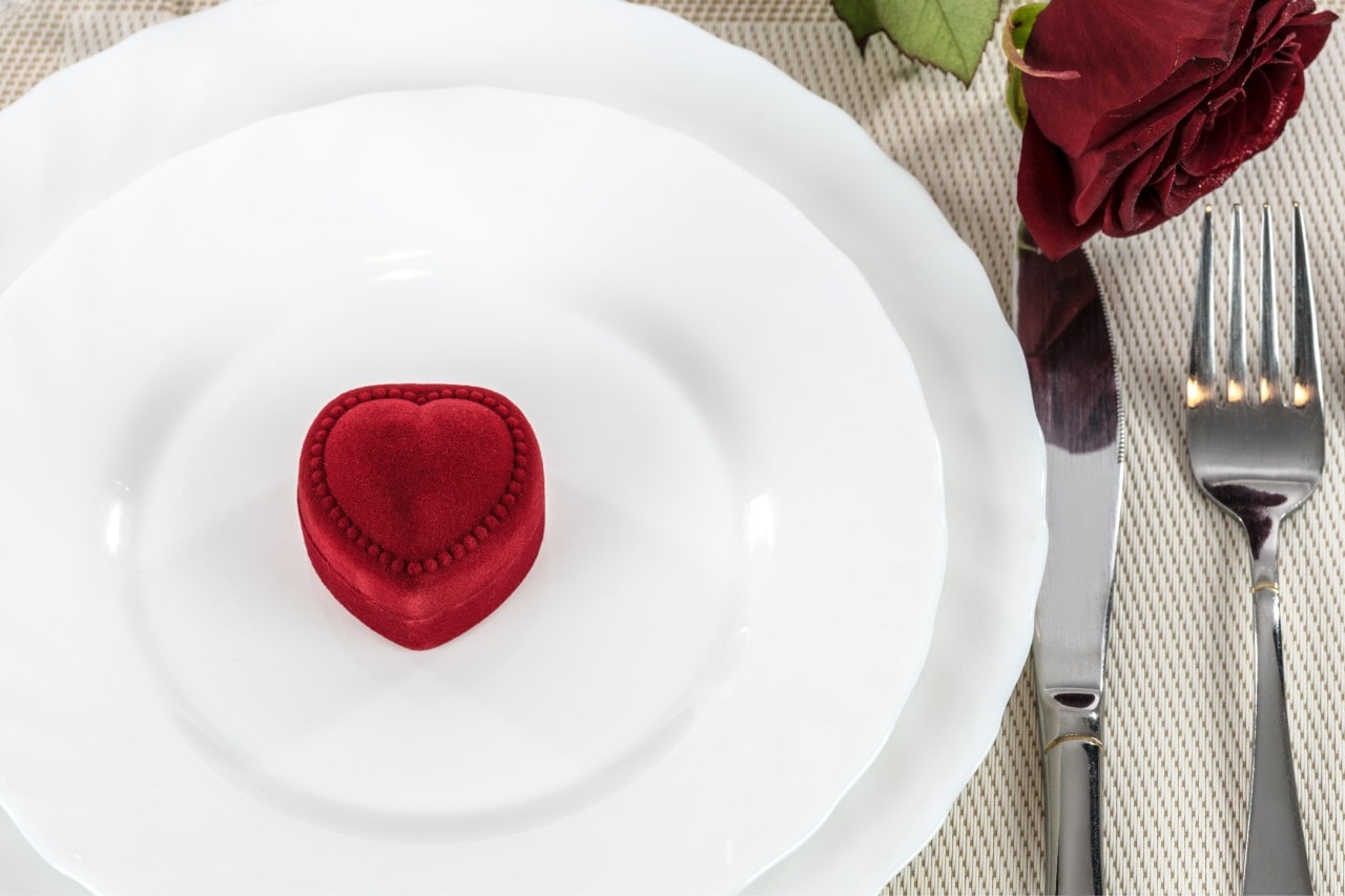 A close-up of a charming velvet jewelry box shaped like a heart, displayed on pristine white dinner plates.