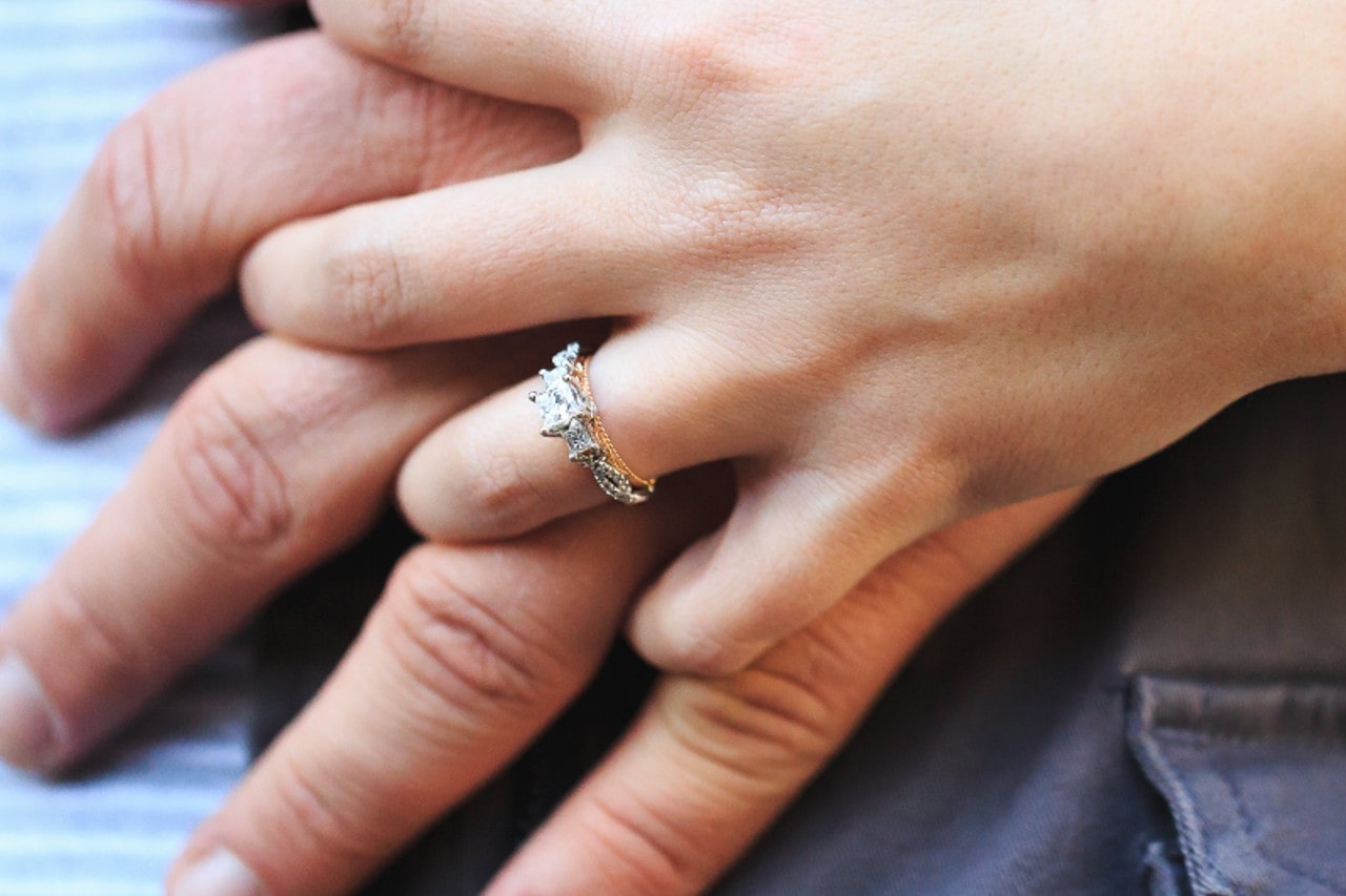 A woman holding a man&rsquo;s hand wears a two-stone three stone ring.