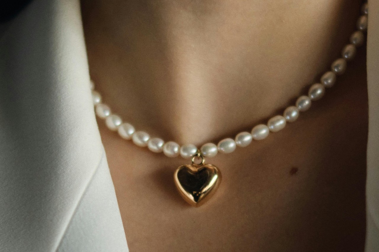 close up image of a woman’s neckline adorned with a pearl necklace with a heart pendant