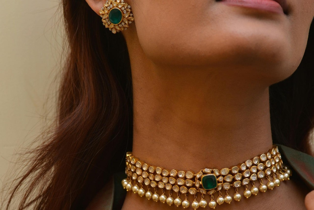 close up image of a woman wearing bold and luxurious gold and emerald jewelry