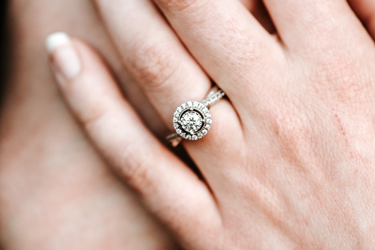 A close up of a white gold halo diamond engagement ring on a woman’s hand