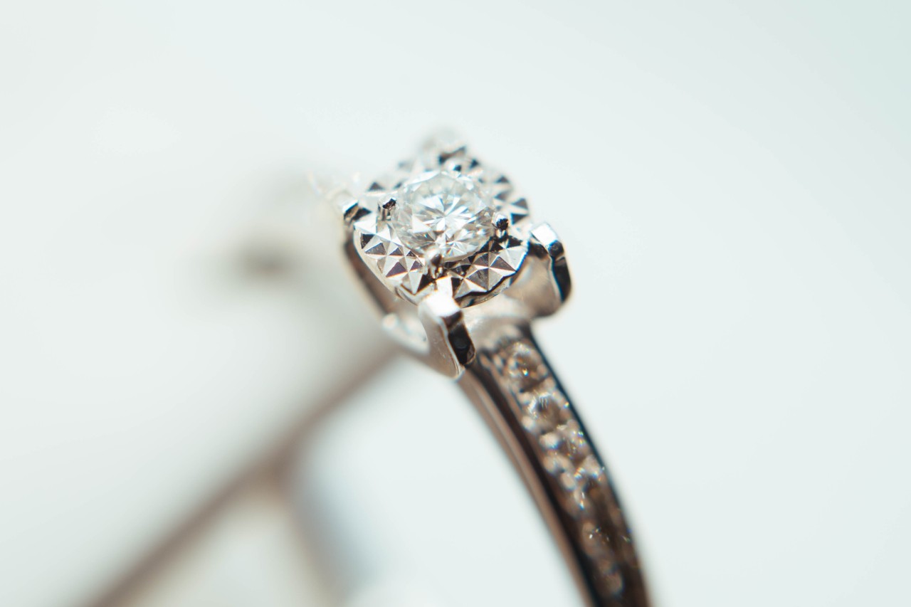 An exquisite white gold engagement ring with a sparkling round brilliant-cut diamond and pavé-accented tapered band, set against a blurred white background