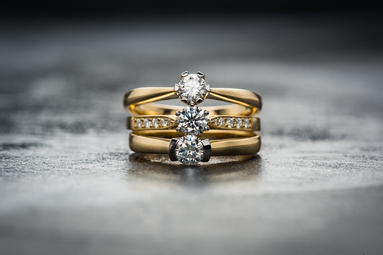 Exquisite stack of gold rings: solitaire, halo, and three-stone center diamond.