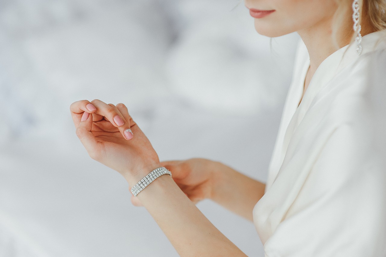 A woman in a beautiful white gown adjusts a sparkling diamond bracelet on her wrist.