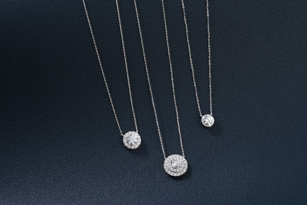 Three silver diamond pendant necklaces on a black textured surface.