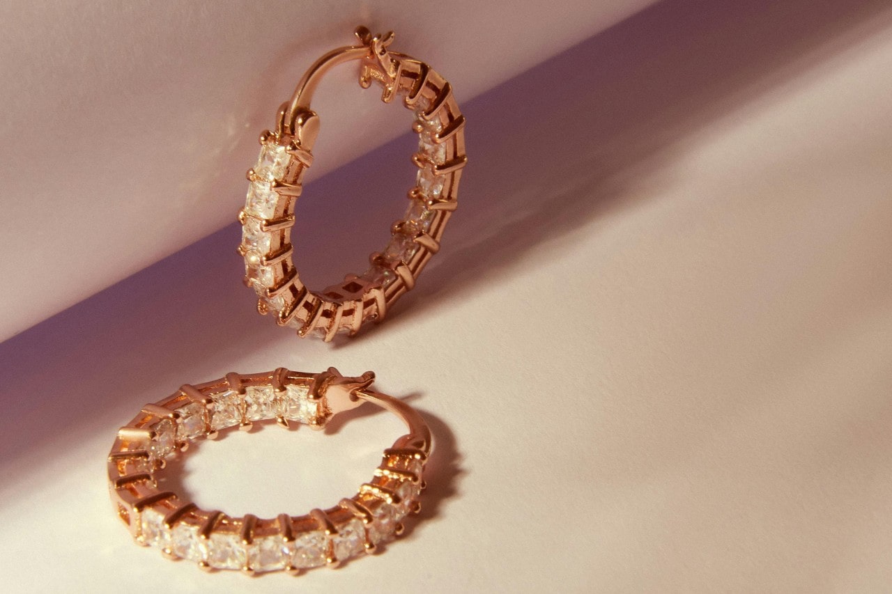 A pair of yellow gold diamond huggie earrings on a beige surface.