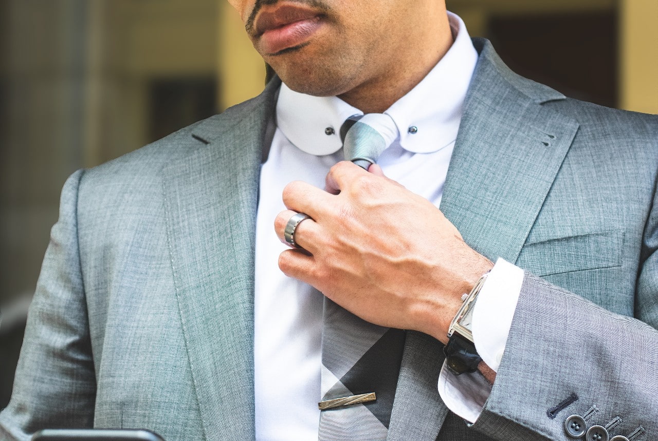 A man in grey suit fixes his tie, showcasing stainless steel wedding band