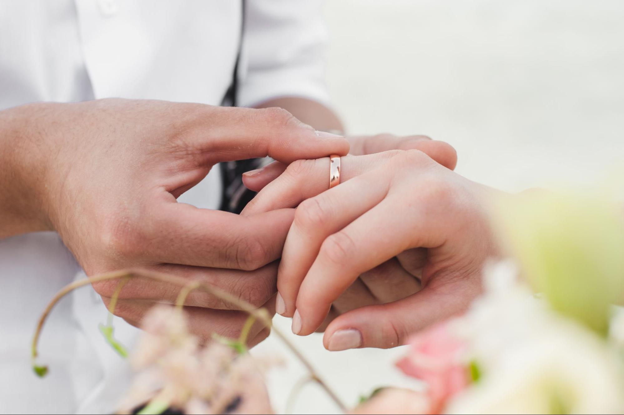 A close up of a hand placing a rose gold polished weeding band onto another hand.