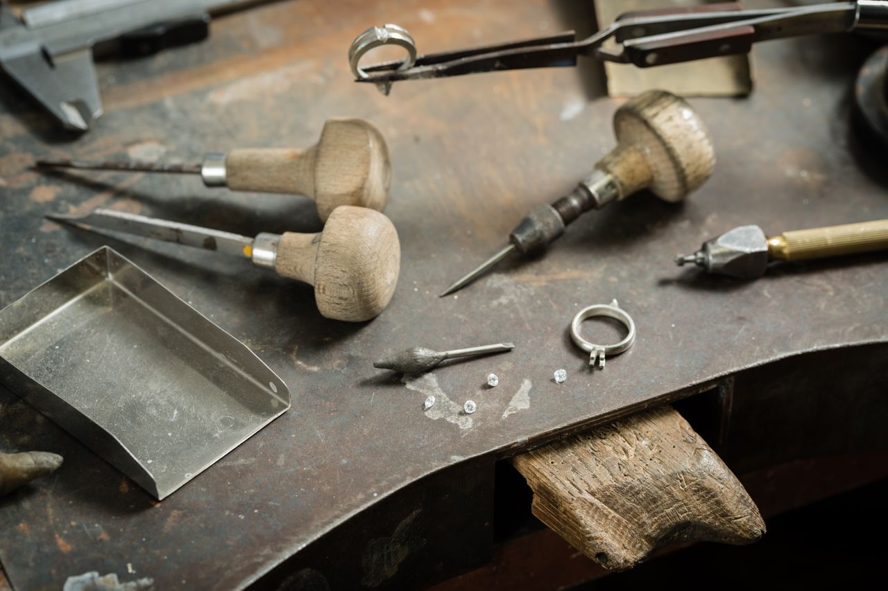 a work desk covered in jewelry-making tools, loose diamonds, and a ring mount a work desk covered in jewelry-making tools, loose diamonds, and a ring mount