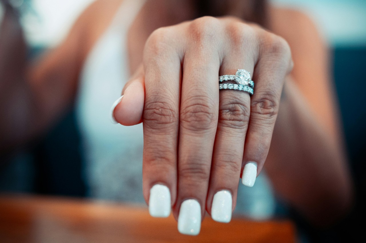 A woman’s extended hand adorned with a diamond engagement ring and matching wedding band. A woman’s extended hand adorned with a diamond engagement ring and matching wedding band.