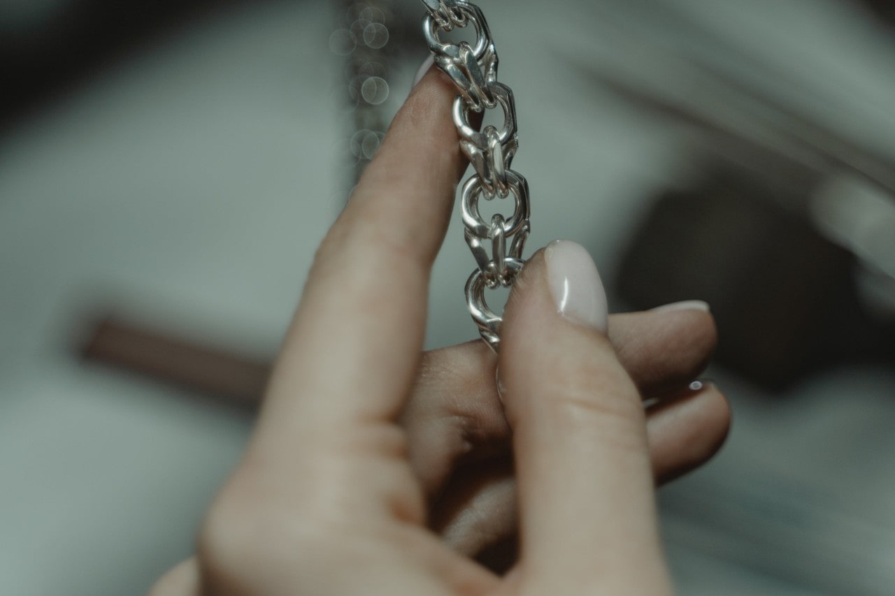 A woman holding a part of a thick silver chain with a blurred, dark background.
