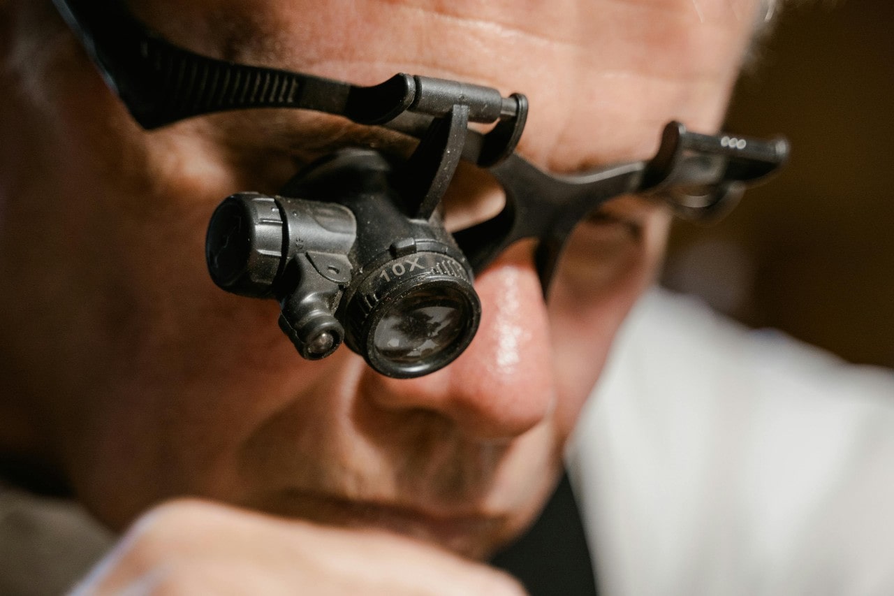 A jewelry expert wearing eye gear, closely examining something out of frame.