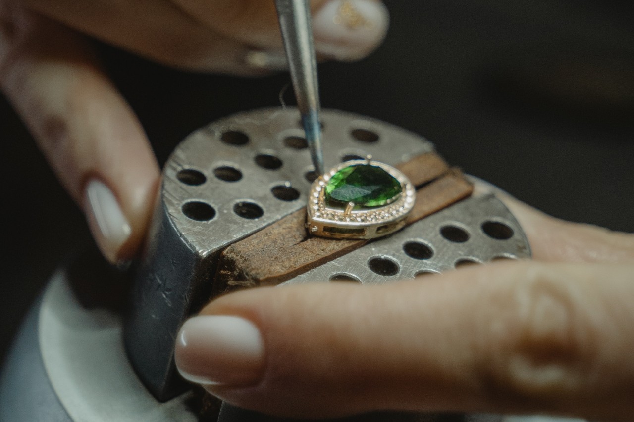 A jewelry professional modifying a pear cut emerald stone with a golden diamond halo.